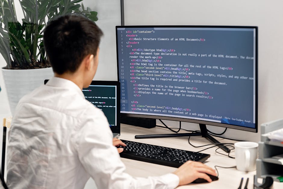 Close-up photograph of a computer screen displaying lines of source code with syntax highlighting, including tags and text in various colours such as red, green, blue, and white on a dark background.